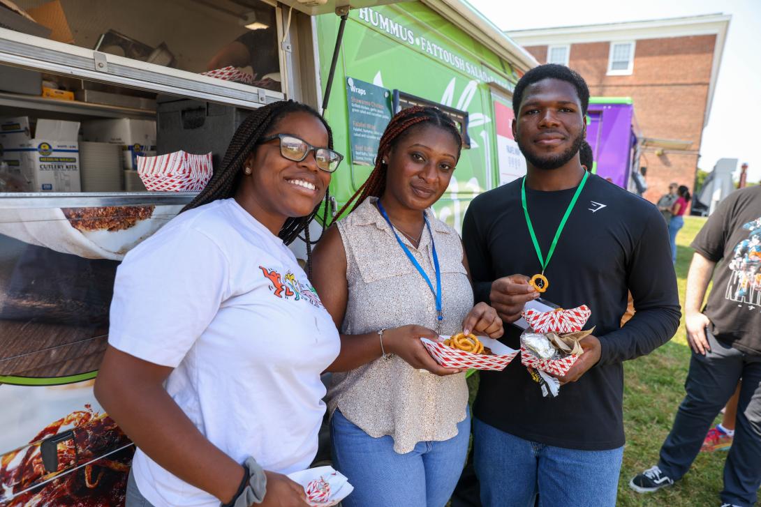 Three students smiling and eating food truck food