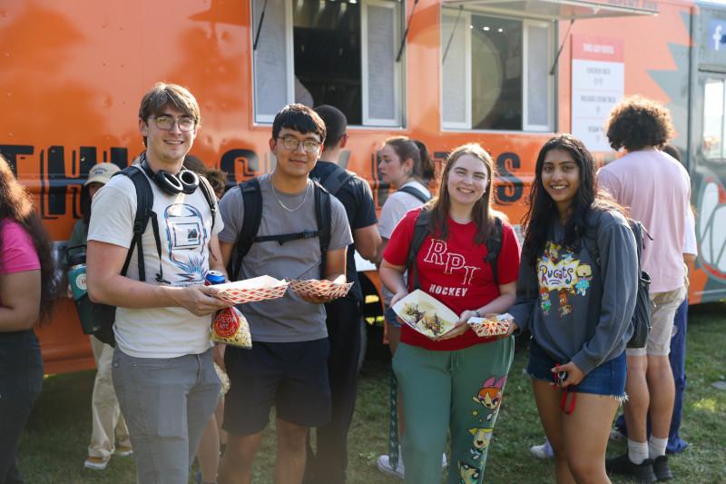Four students smiling and enjoying food from food truck